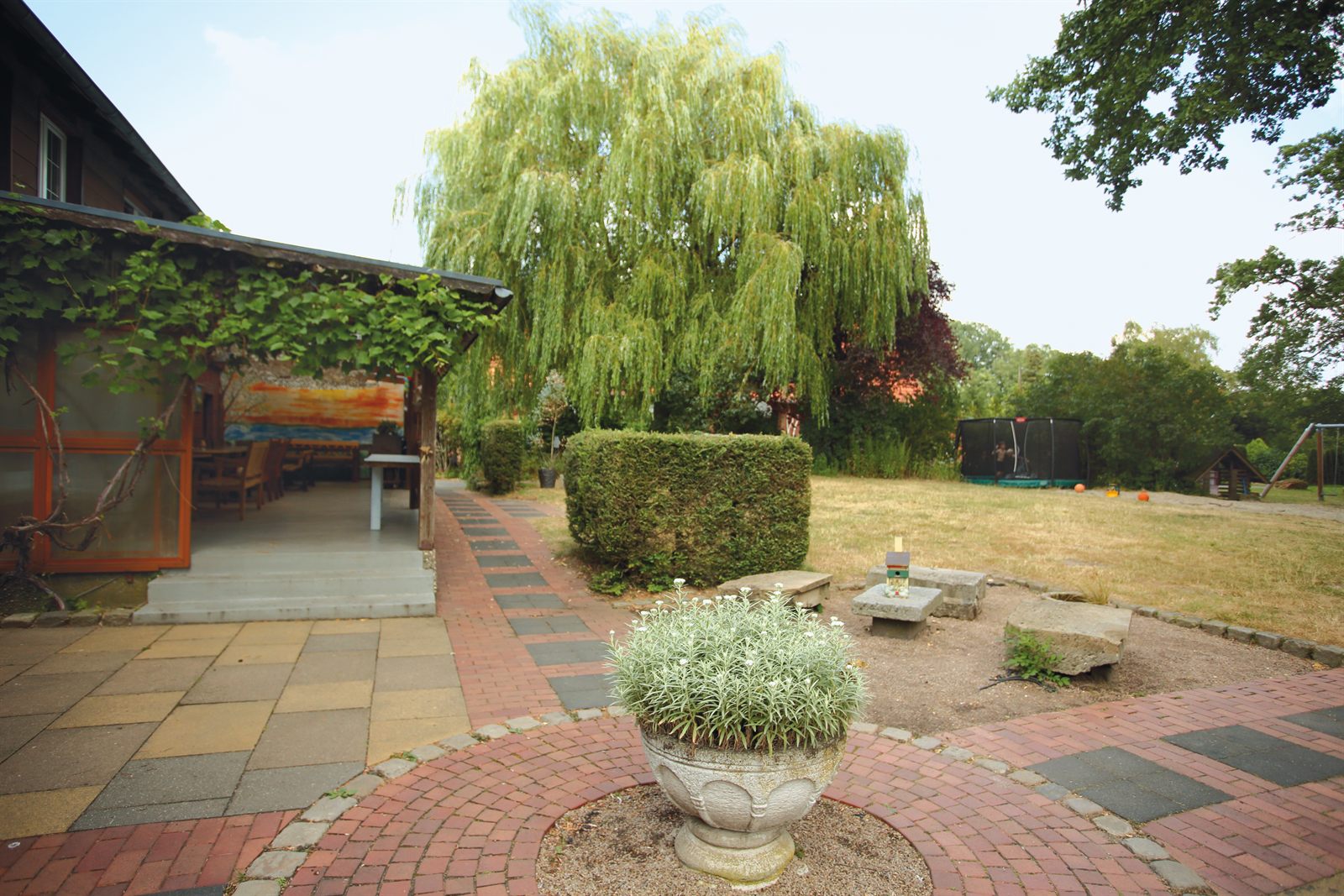 Blick auf Terrasse, Steinecke, Wiese, Trampolin und Spielplatz